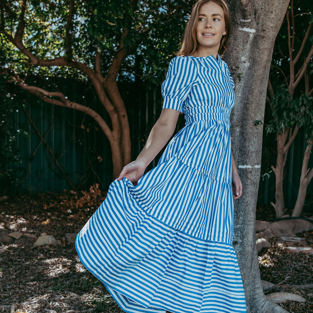 Woman in a blue and white striped dress standing next to a tree in a natural setting
