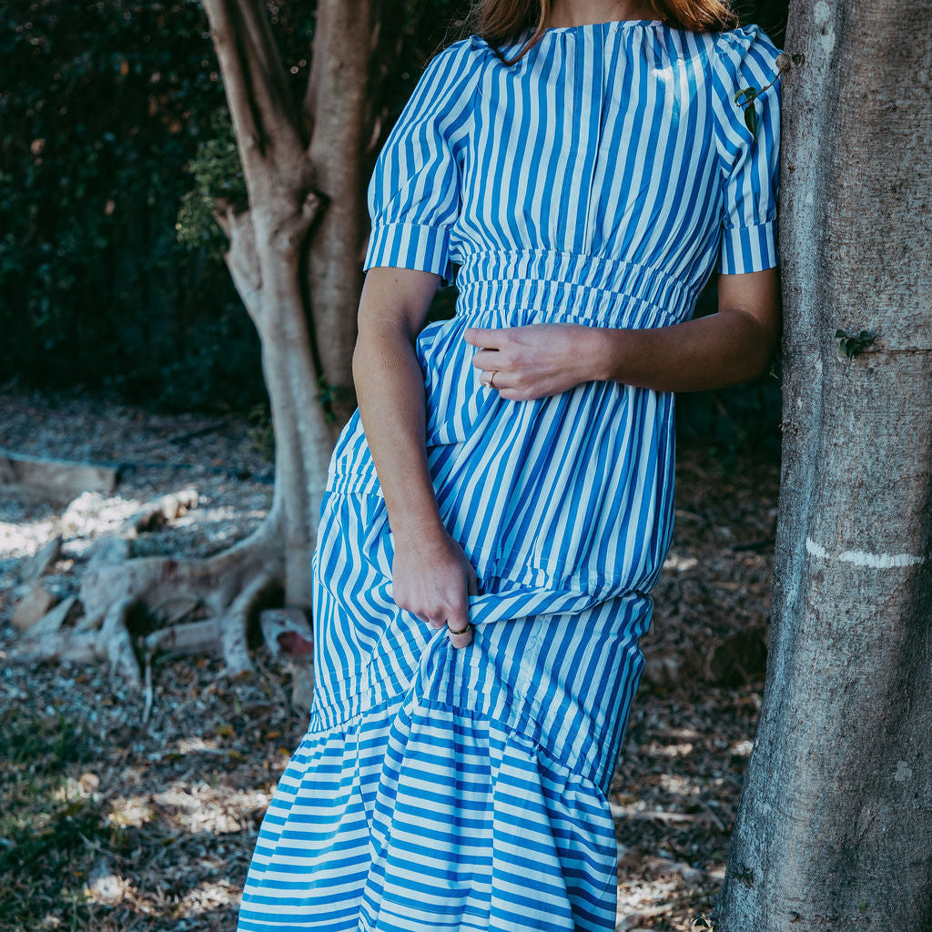 Woman in a blue and white striped dress standing next to a tree in a natural setting