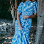Woman in a blue and white striped dress standing next to a tree in a natural setting