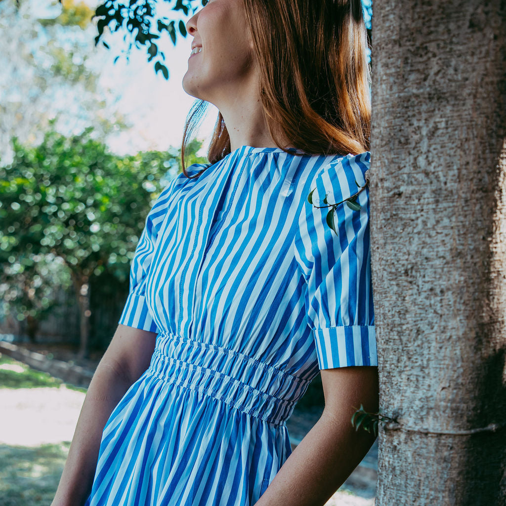 Woman in a blue and white striped dress standing next to a tree
