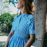 Woman in a blue and white striped dress standing next to a tree