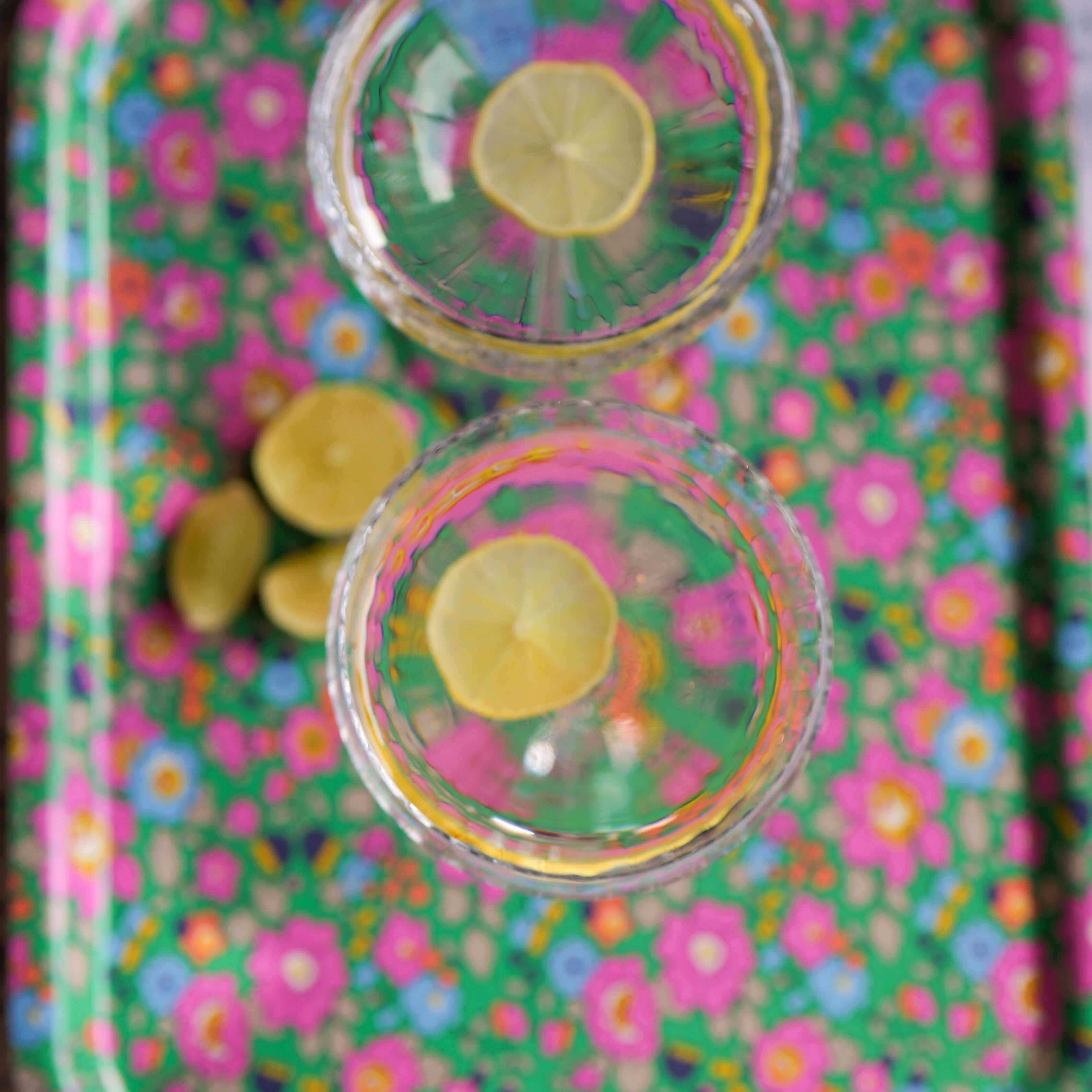 Colorful floral-patterned tray with small round containers and lemons on a textured surface.