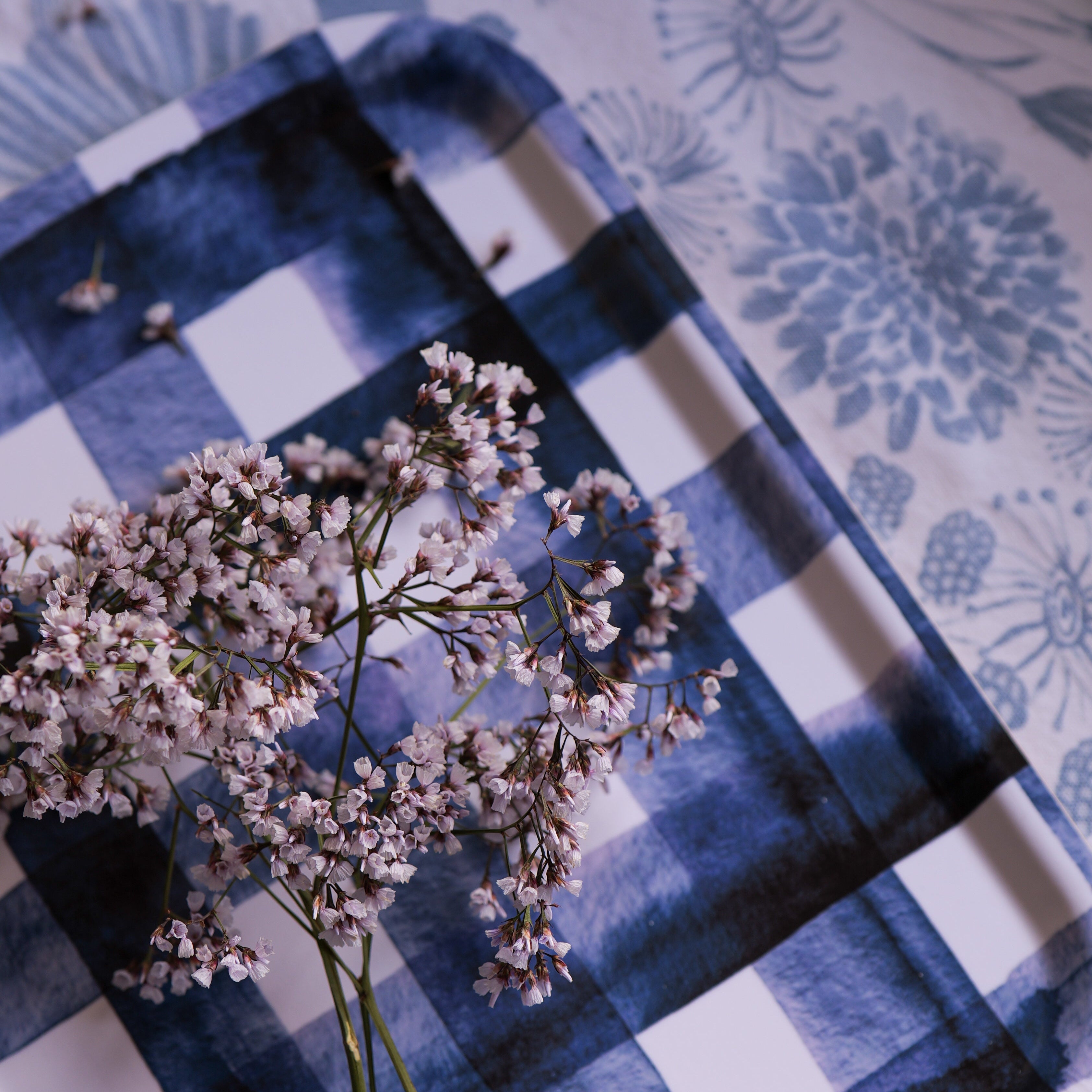Blue and white checkered towel with dried flowers on a floral-patterned surface