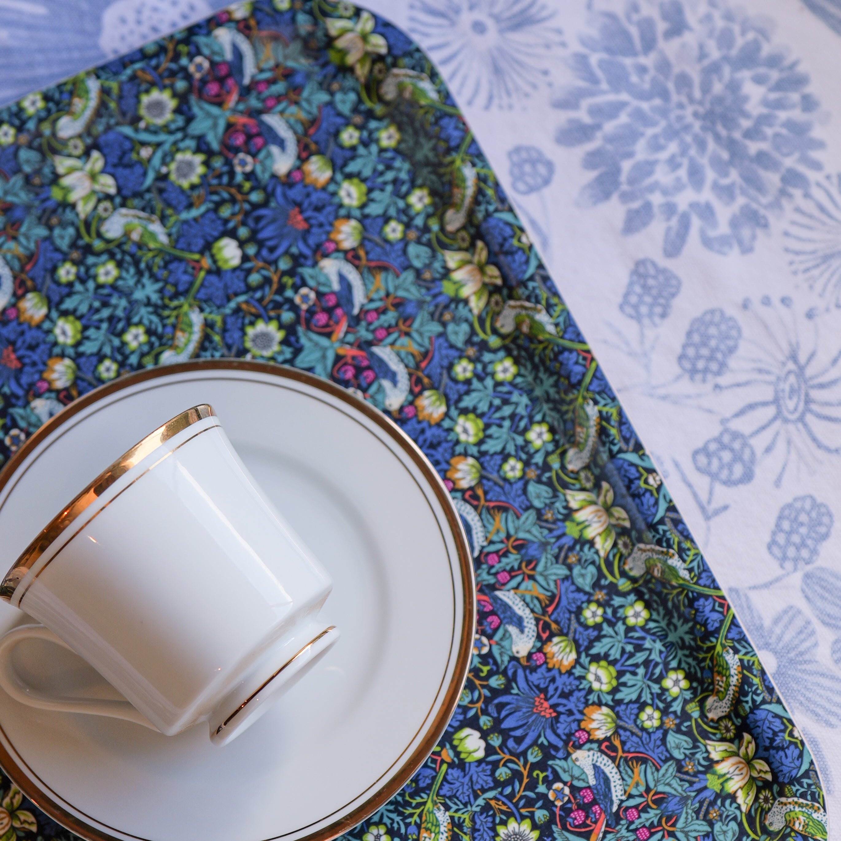 Ceramic cup and saucer on a floral placemat with a white floral tablecloth background