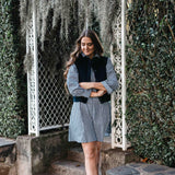 Woman in checkered dress with black vest standing in a garden.
