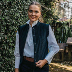 Woman wearing a dark green vest over a white shirt in a garden setting.