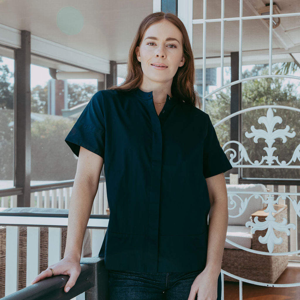 Woman standing on a balcony wearing a navy shirt and jeans.