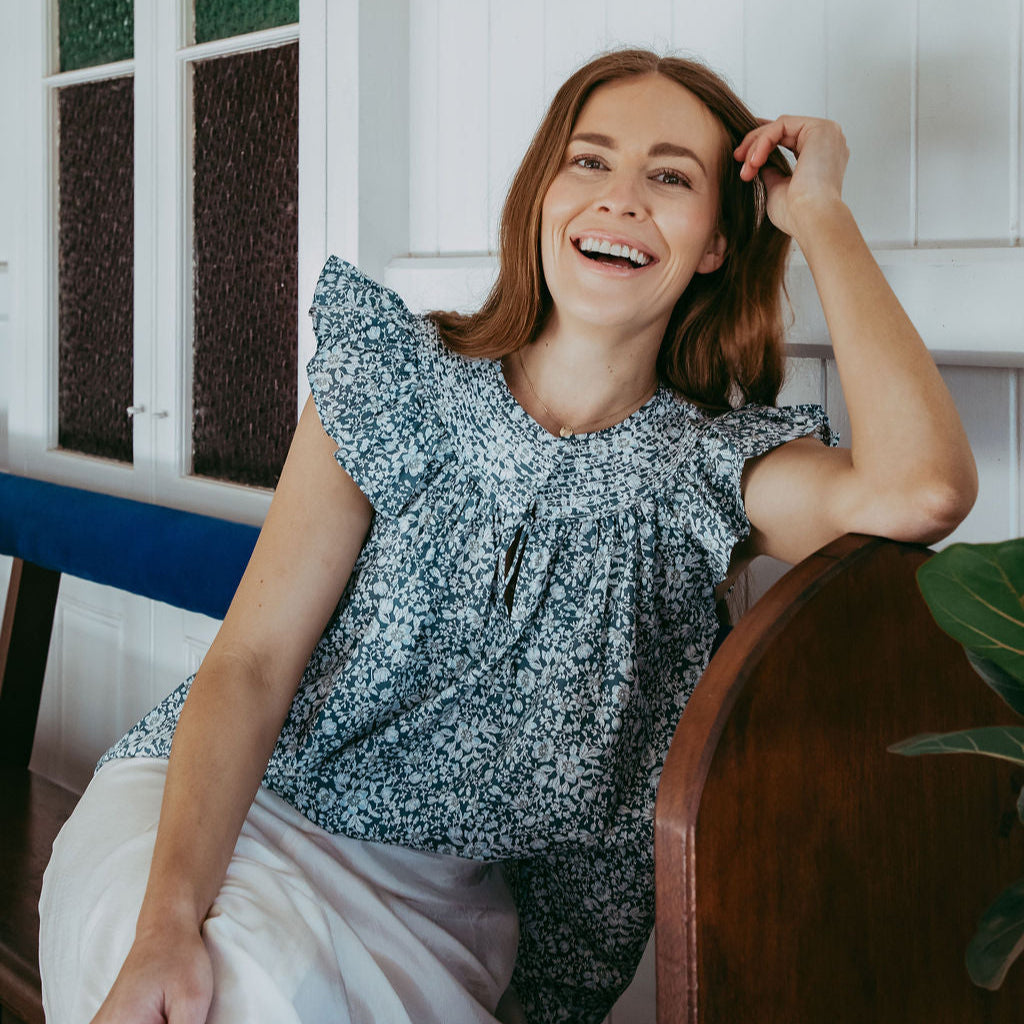 Woman sitting on a wooden chair indoors, smiling.