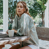 Woman sitting at a wooden table outdoors, holding a mug.