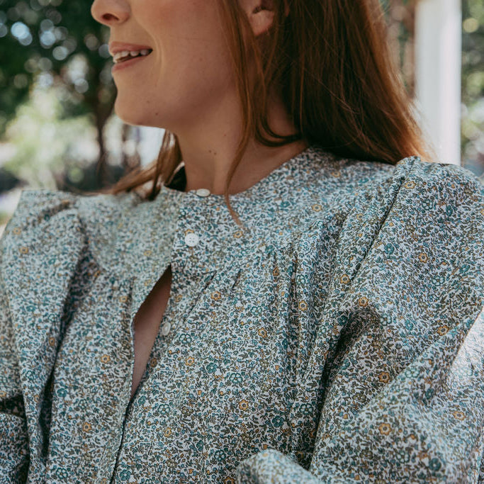 Woman wearing a floral blouse sitting outdoors with blurred background