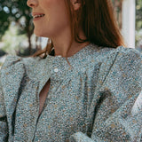Woman wearing a floral blouse sitting outdoors with blurred background