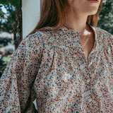 Person wearing a floral blouse standing outdoors with greenery in the background
