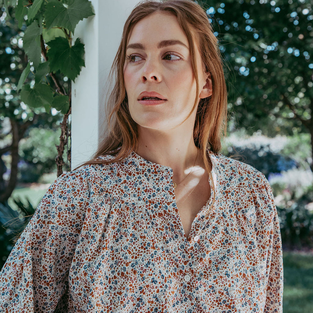 Woman wearing a floral blouse standing outdoors with greenery in the background