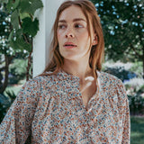 Woman wearing a floral blouse standing outdoors with greenery in the background