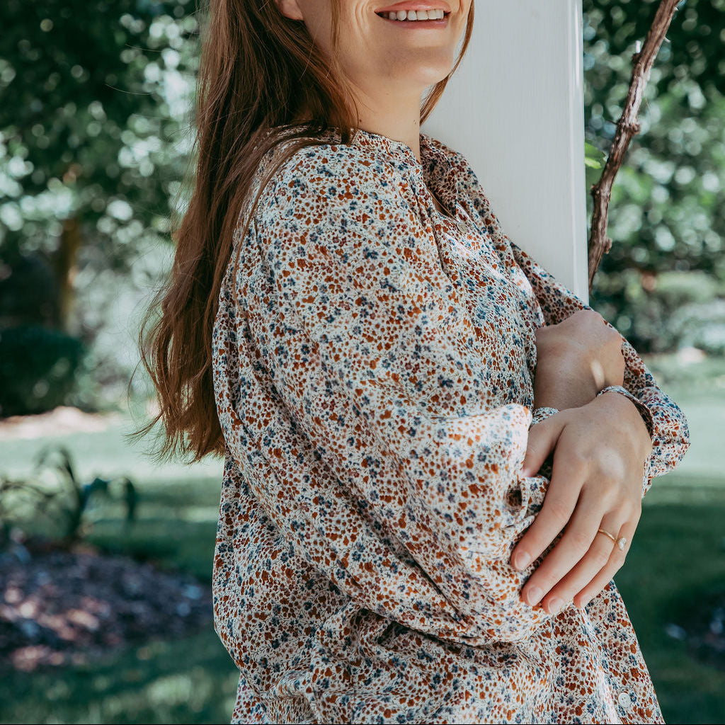 Woman in a floral dress standing outdoors with trees in the background