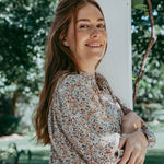 Woman in a floral dress standing outdoors with trees in the background