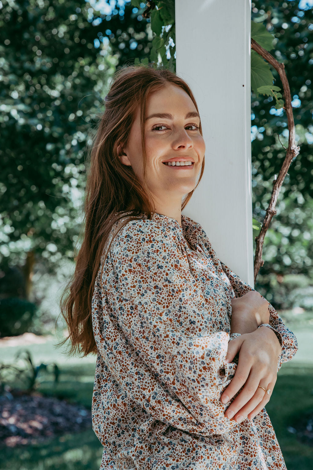 Woman in a floral dress standing outdoors with trees in the background