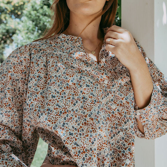 Person wearing a floral blouse with a blurred outdoor background
