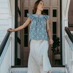 Woman standing on a staircase wearing a blue floral top and white pants.