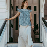 Woman standing on a staircase wearing a blue floral top and white pants.