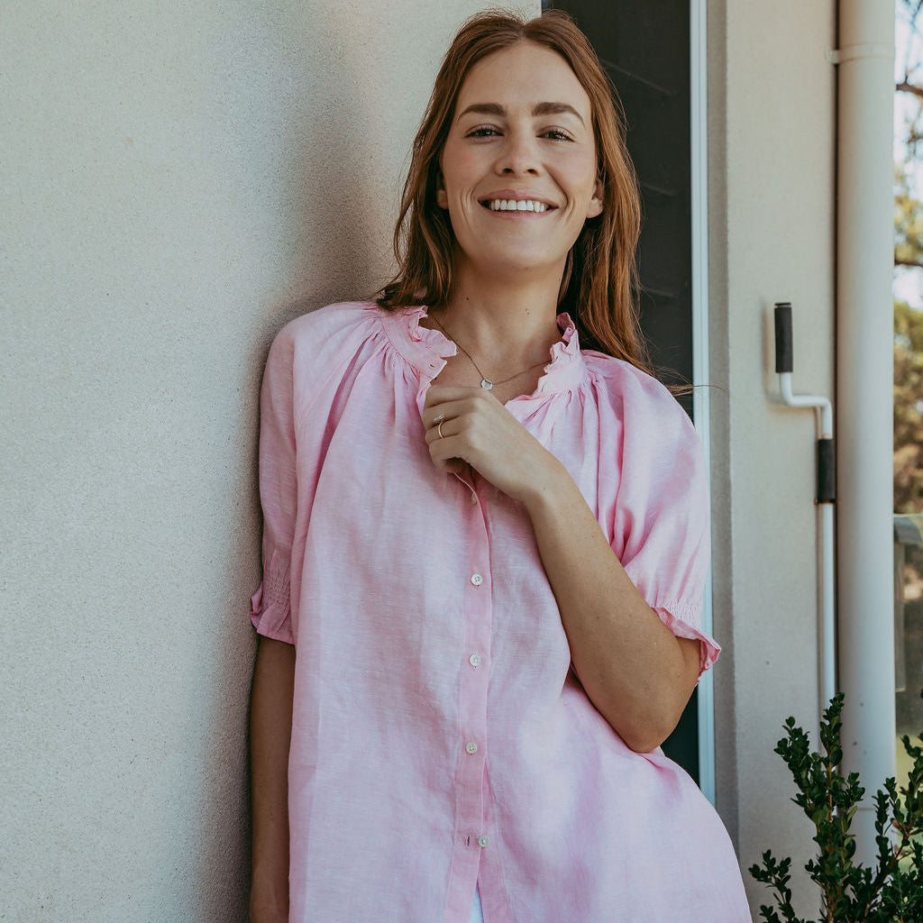 Woman in a pink shirt standing against a wall indoors