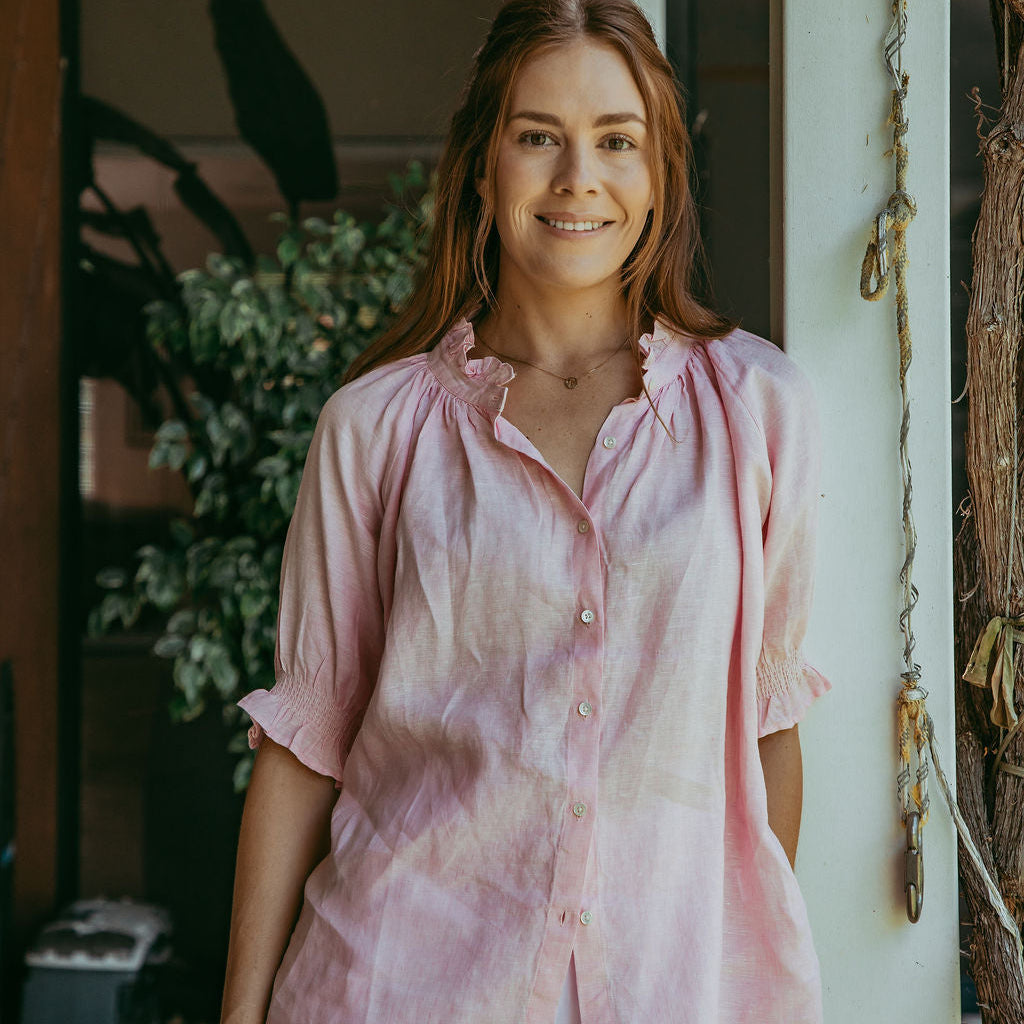 Woman wearing a pink tie-dye shirt standing in a casual setting with plants in the background