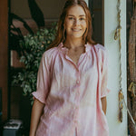 Woman wearing a pink tie-dye shirt standing in a casual setting with plants in the background