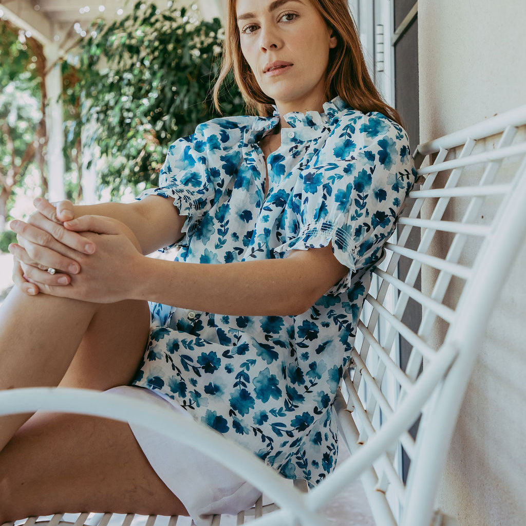 Woman in a floral dress sitting on a white chair outdoors.