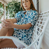 Woman in a floral dress sitting on a white chair outdoors.