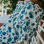 Woman wearing a blue floral dress sitting outdoors with blurred background
