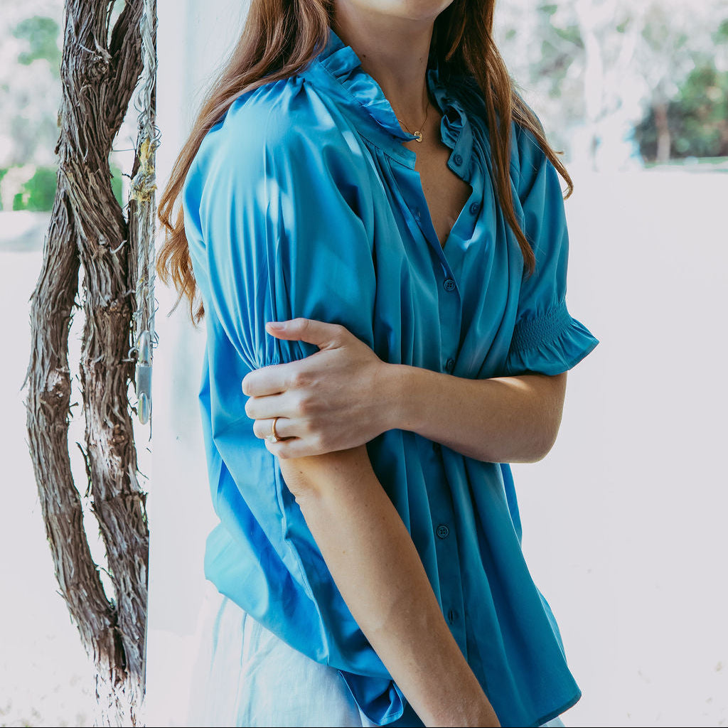 Woman wearing a blue shirt standing outdoors with blurred background