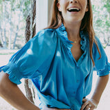 Woman wearing a blue blouse outdoors with trees and sunlight in the background