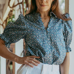 Woman wearing a blue floral blouse and white shorts outdoors.