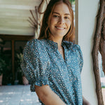 Woman wearing a blue floral blouse and white pants standing outdoors.