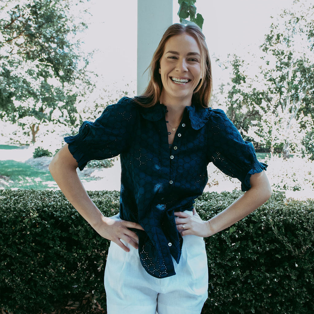 Woman standing outdoors with greenery and a pool in the background