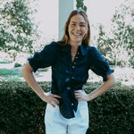 Woman standing outdoors with greenery and a pool in the background