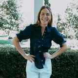 Woman standing outdoors with greenery and a pool in the background