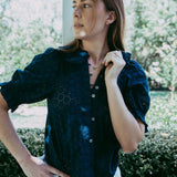 Woman wearing a dark blue blouse with a blurred garden background