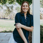 Woman in a blue shirt and white shorts standing outdoors under a gazebo.