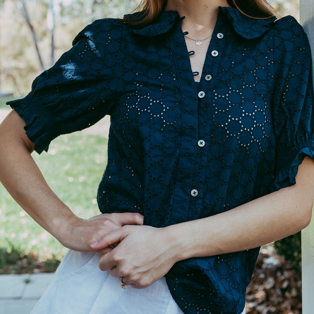 Woman wearing a dark blue blouse with white buttons outdoors