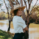 Woman wearing a straw hat and white blouse by a river