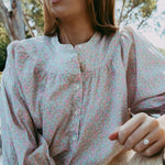 Woman wearing a floral blouse sitting outdoors with trees in the background