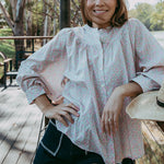 Woman in a light blouse and shorts standing outdoors with trees and a lake in the background