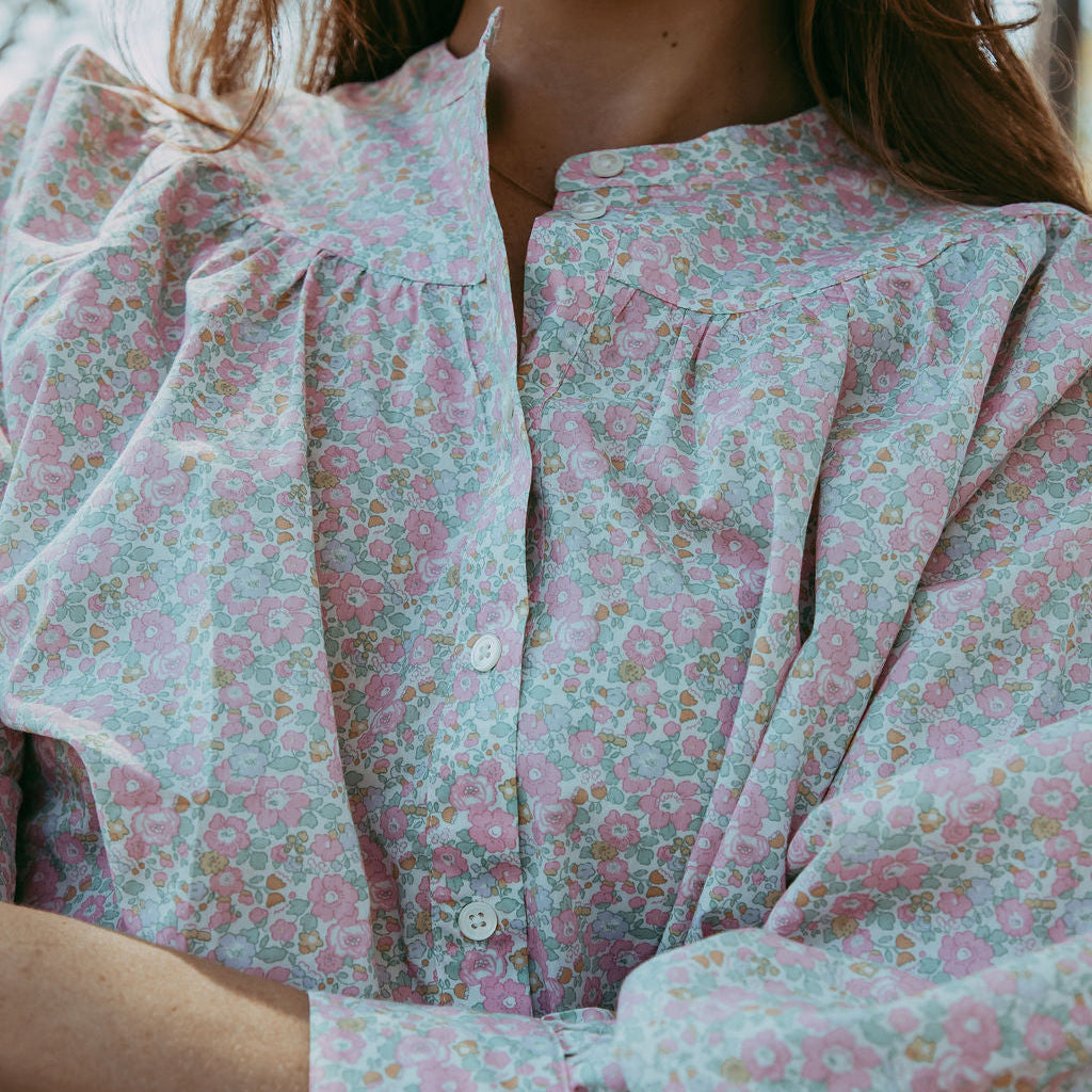 Close-up of a person wearing a floral blouse with long sleeves.