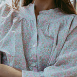 Close-up of a person wearing a floral blouse with long sleeves.