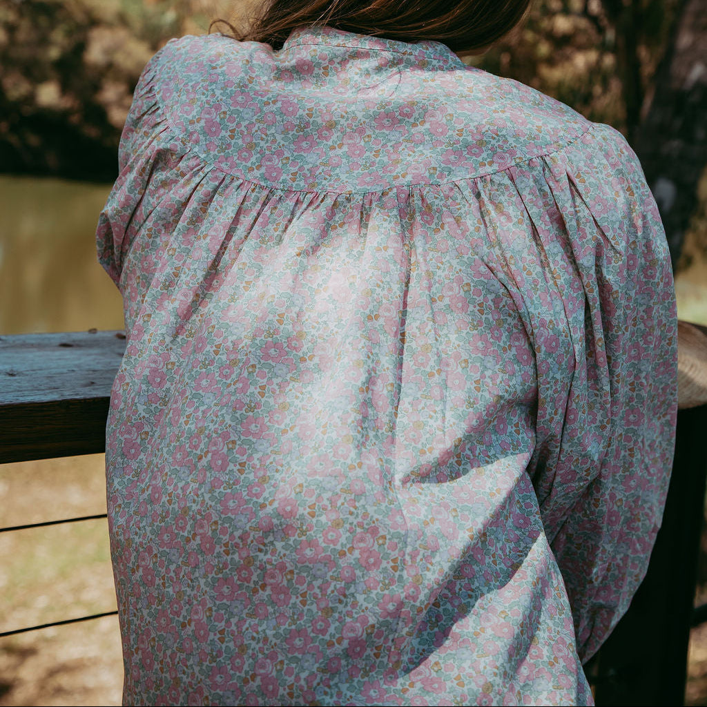 Person wearing a floral blouse standing outdoors with trees in the background