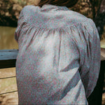 Person wearing a floral blouse standing outdoors with trees in the background