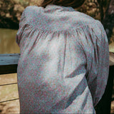 Person wearing a floral blouse standing outdoors with trees in the background