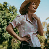 Woman wearing a straw hat and floral blouse outdoors with trees in the background