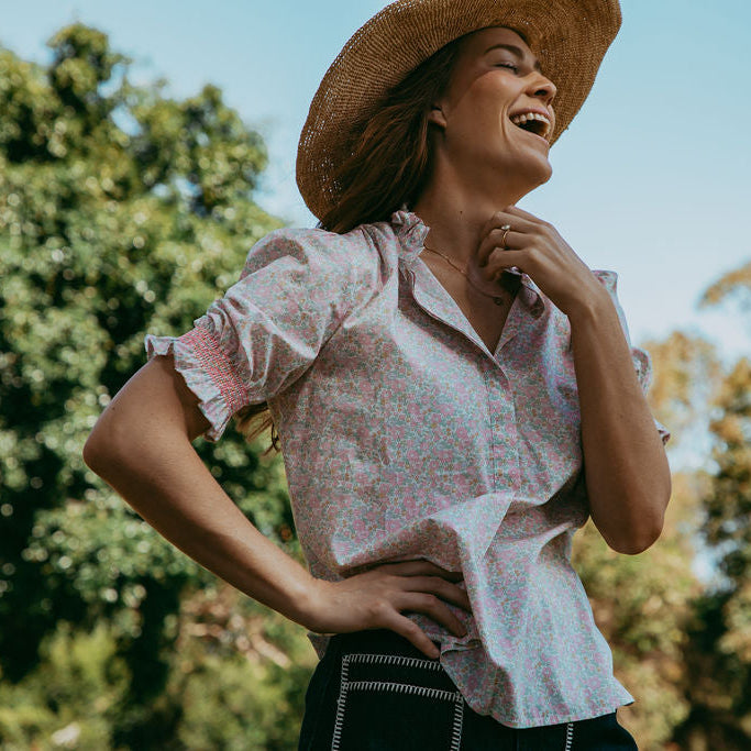 Woman wearing a straw hat and floral blouse outdoors with trees in the background